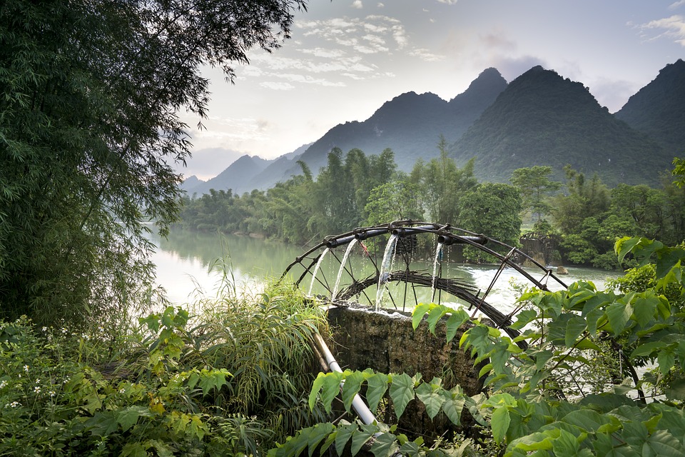 Rustic footbridge remains over a tranquil river with lush greenery and mountains in the background, showcasing the area's serene climate.