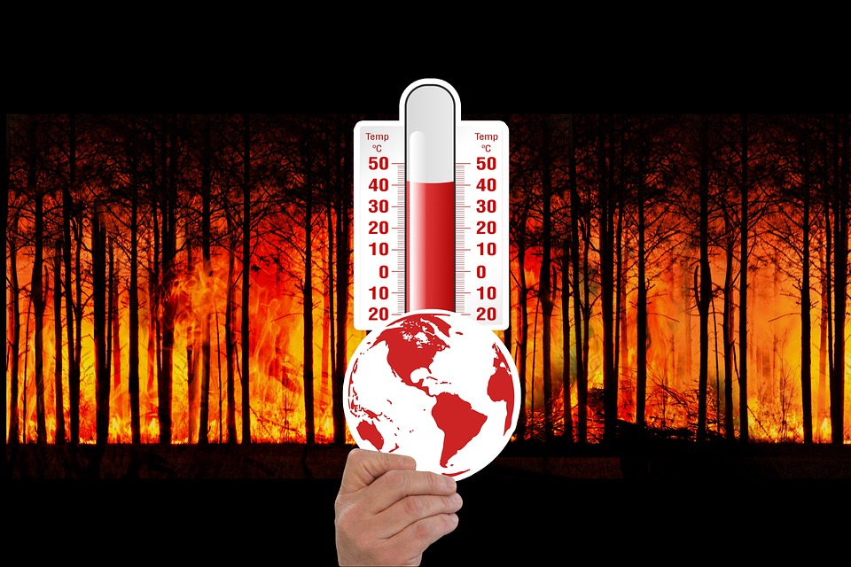 Conceptual image of a hand holding the earth with a background of forest fires and temperature gauges indicating rising global temperatures due to climate change.