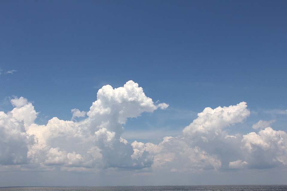 Cumulus clouds over a tranquil sea under a blue sky reflect the gentle climate.