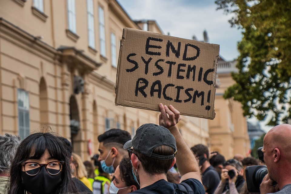 Protester holding a sign that reads "end climate racism!" in a crowd.