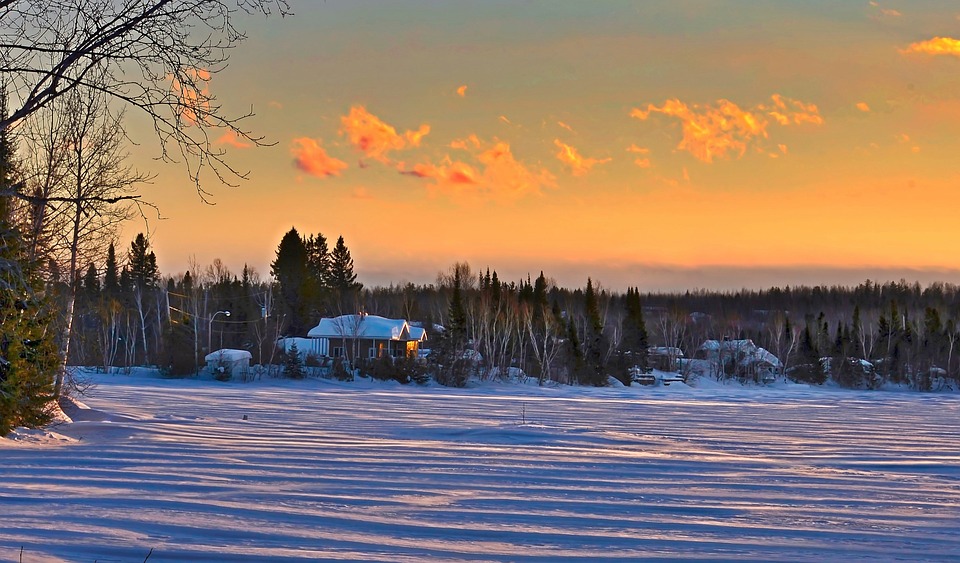 Climate-affected snow-covered landscape with a house during a golden sunrise.