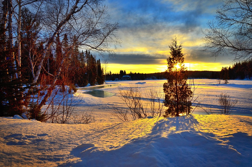Winter sunset over a snow-covered landscape with trees and a frozen river, reflecting the climate's influence.