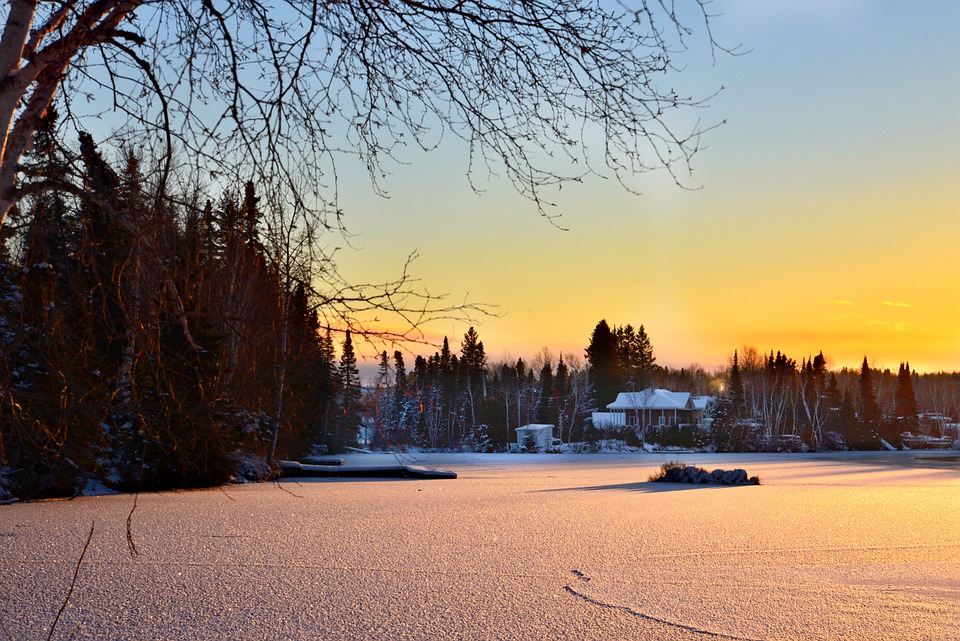 Winter sunrise over a climate-influenced snow-covered landscape with a frozen lake and houses in the distance.