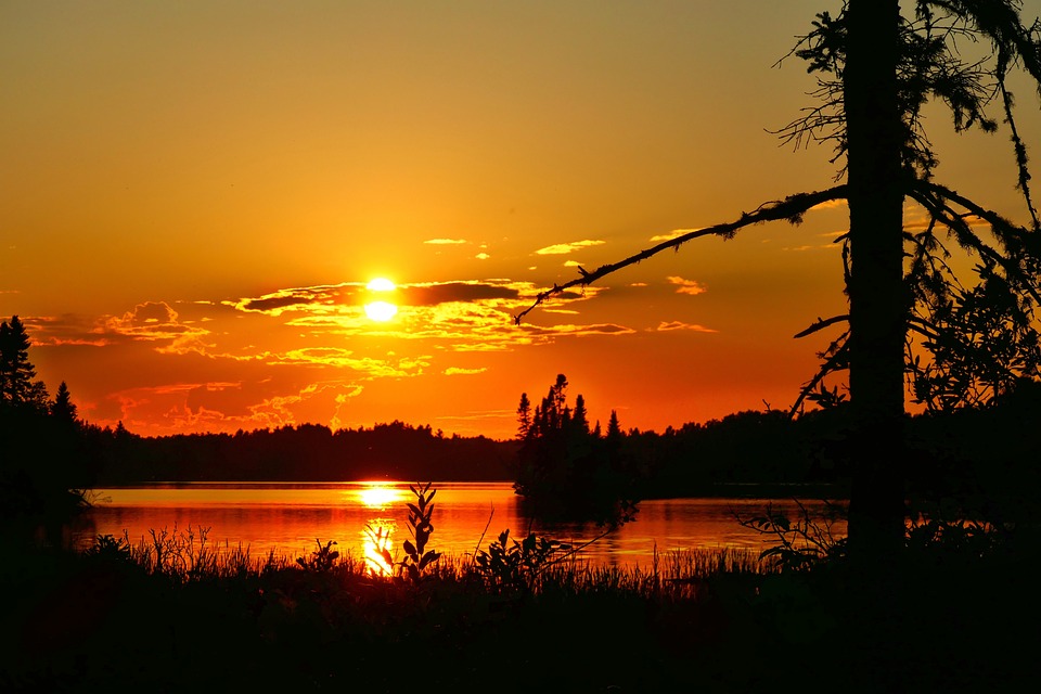 Sunset over a tranquil lake with the silhouette of trees against a vibrant orange sky reflects the climate's serenity.