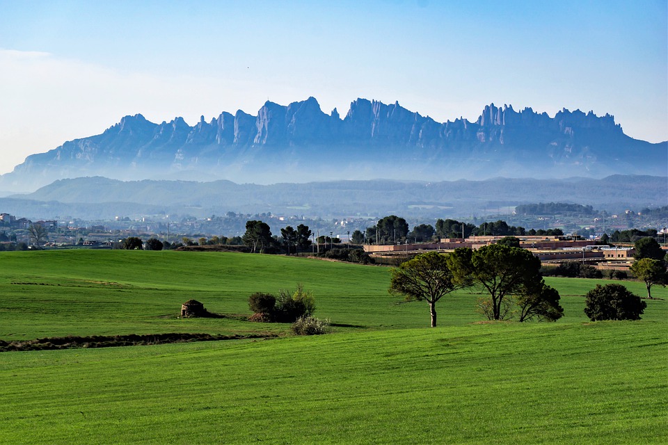 Rolling green fields lead to a distant mountain range under a clear blue sky, shaped by the climate.