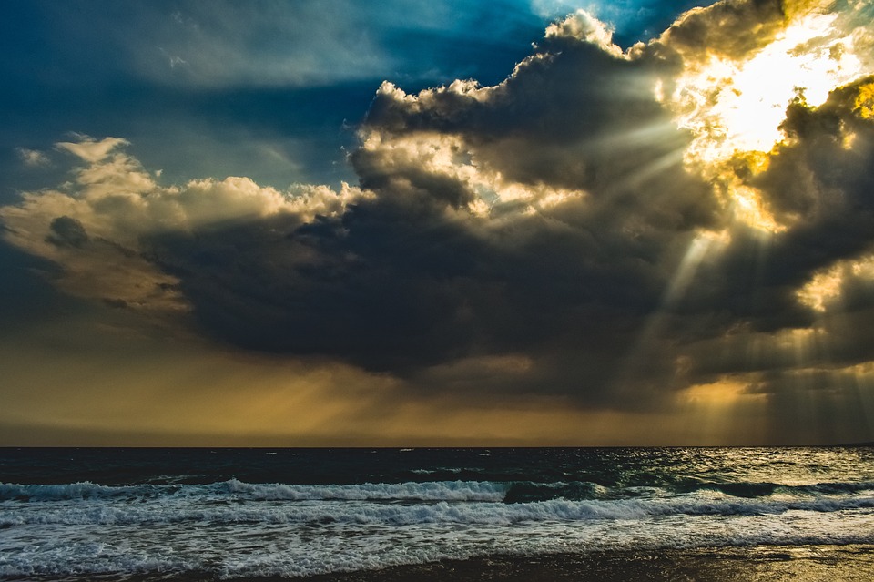Sunlight piercing through storm clouds over a turbulent sea amidst changing climate conditions.