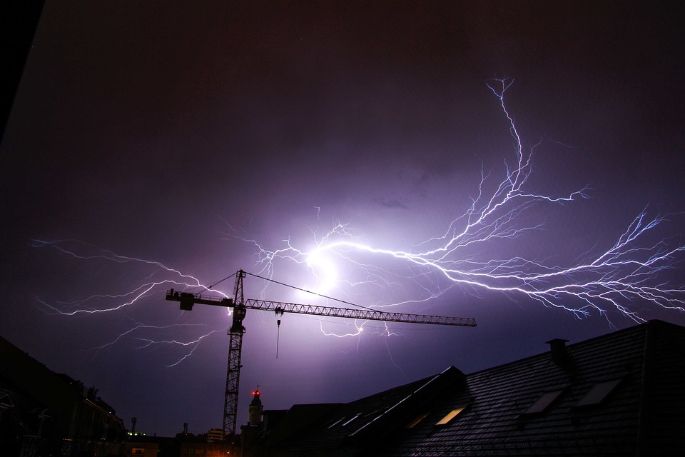 Lightning streaks illuminate the night sky above an urban landscape with a construction crane, hinting at the volatile climate.